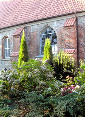 Grüne Friedhofs-Pflanzen und Grabsteine vor der roten Backsteinkirche