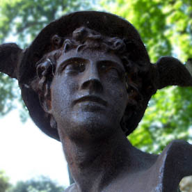 Steinerne Figur des Hermes vor günen Bäumen
